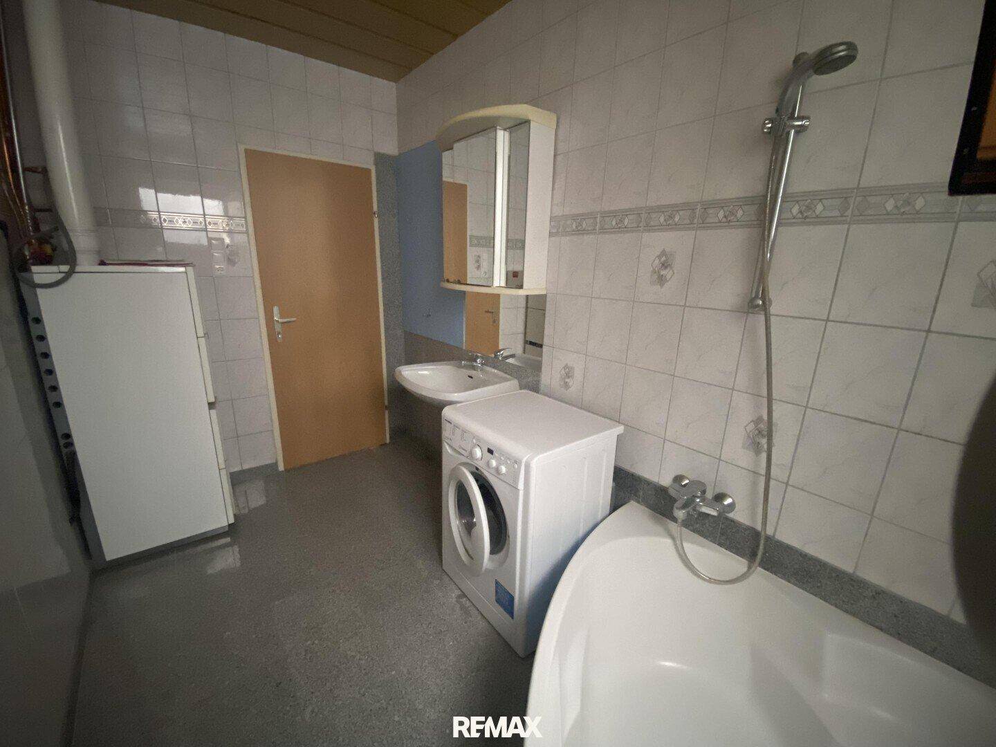 Badezimmer mit Badewanne, Waschbecken, Waschmaschine und hell gefliesten Wänden.