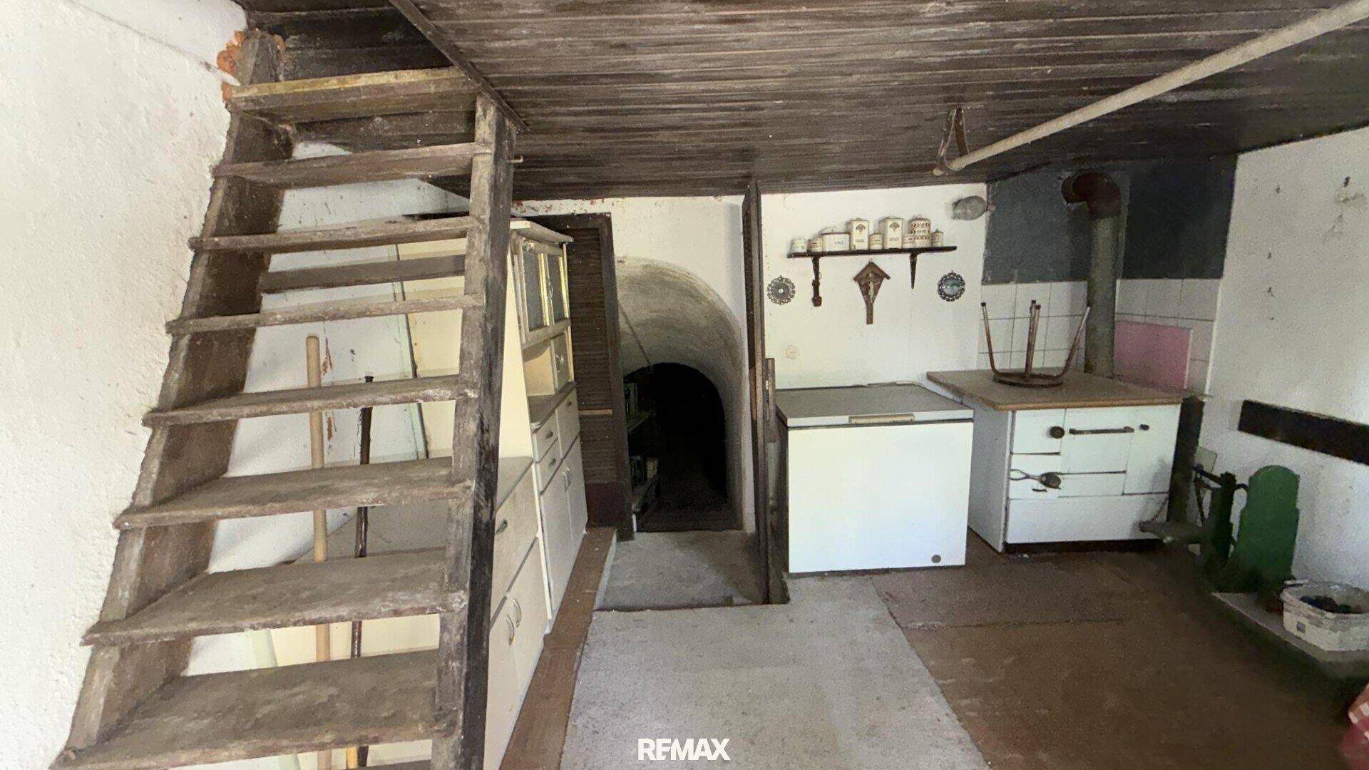 Rustikaler Kellerraum mit Holztreppe, alter Kochstelle und Gefriertruhe.