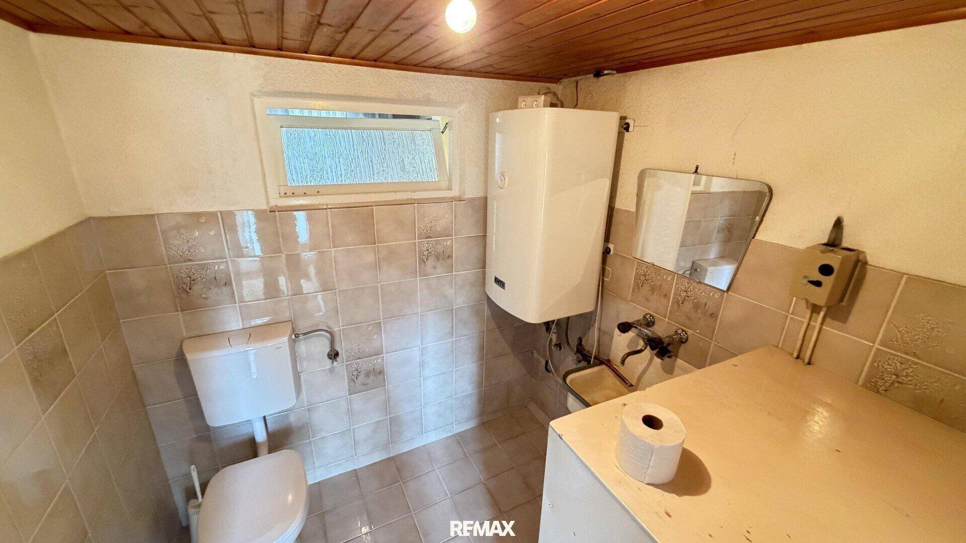 Einfaches WC mit Fenster, Boiler und halbhoch gefliesten Wänden.