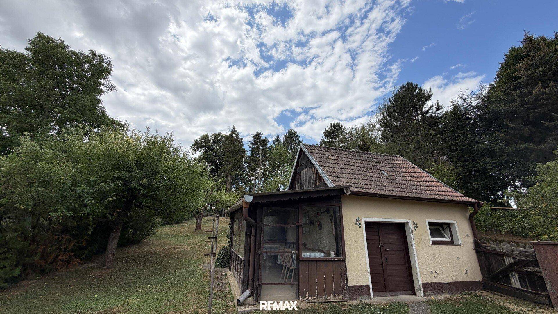 Kleines Nebengebäude mit Veranda in einem weitläufigen Garten.