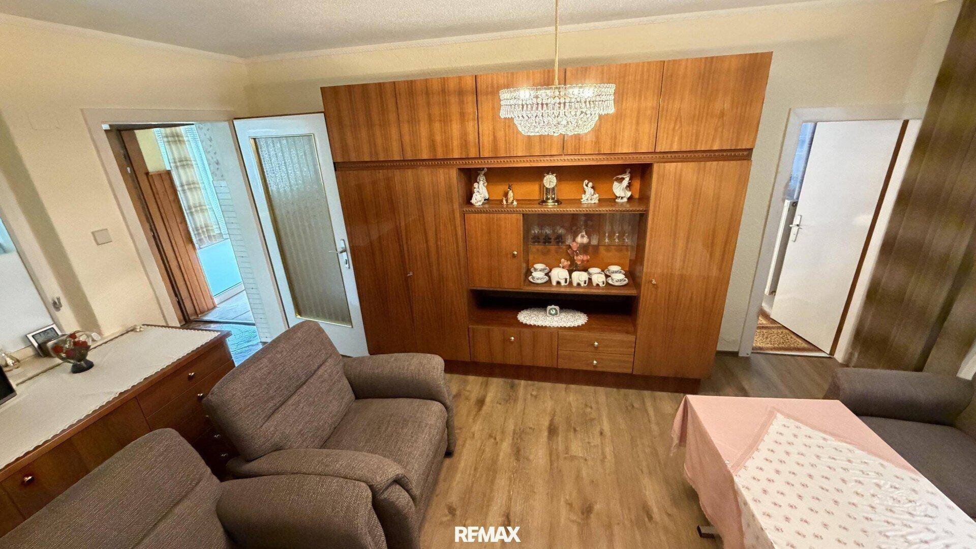 Wohnzimmer mit großer Holzschrankwand, bequemen Sesseln und Laminatboden.