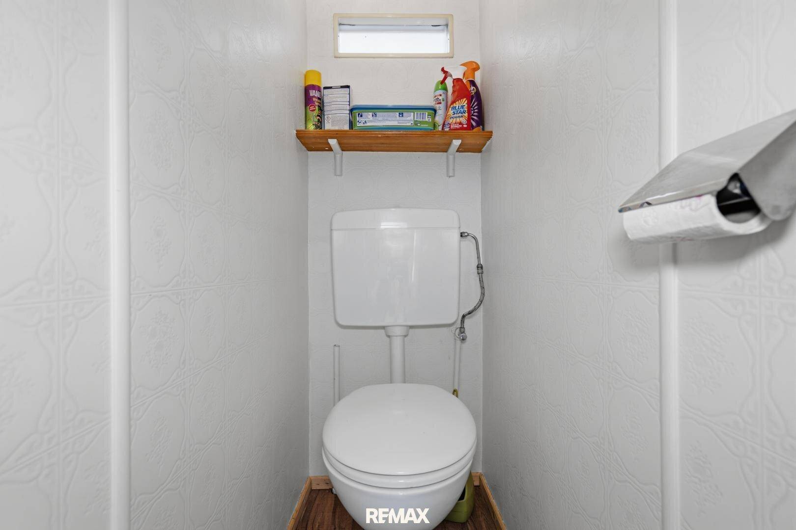 Separate Toilette mit WC, kleinem Fenster und einer Ablage über dem Spülkasten.