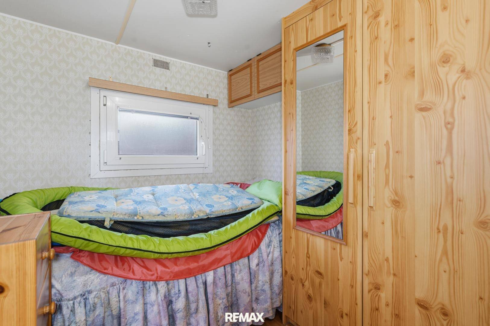 Nahaufnahme des Bettes und des Holzschranks mit Spiegel in einem Schlafzimmer mit Fenster.
