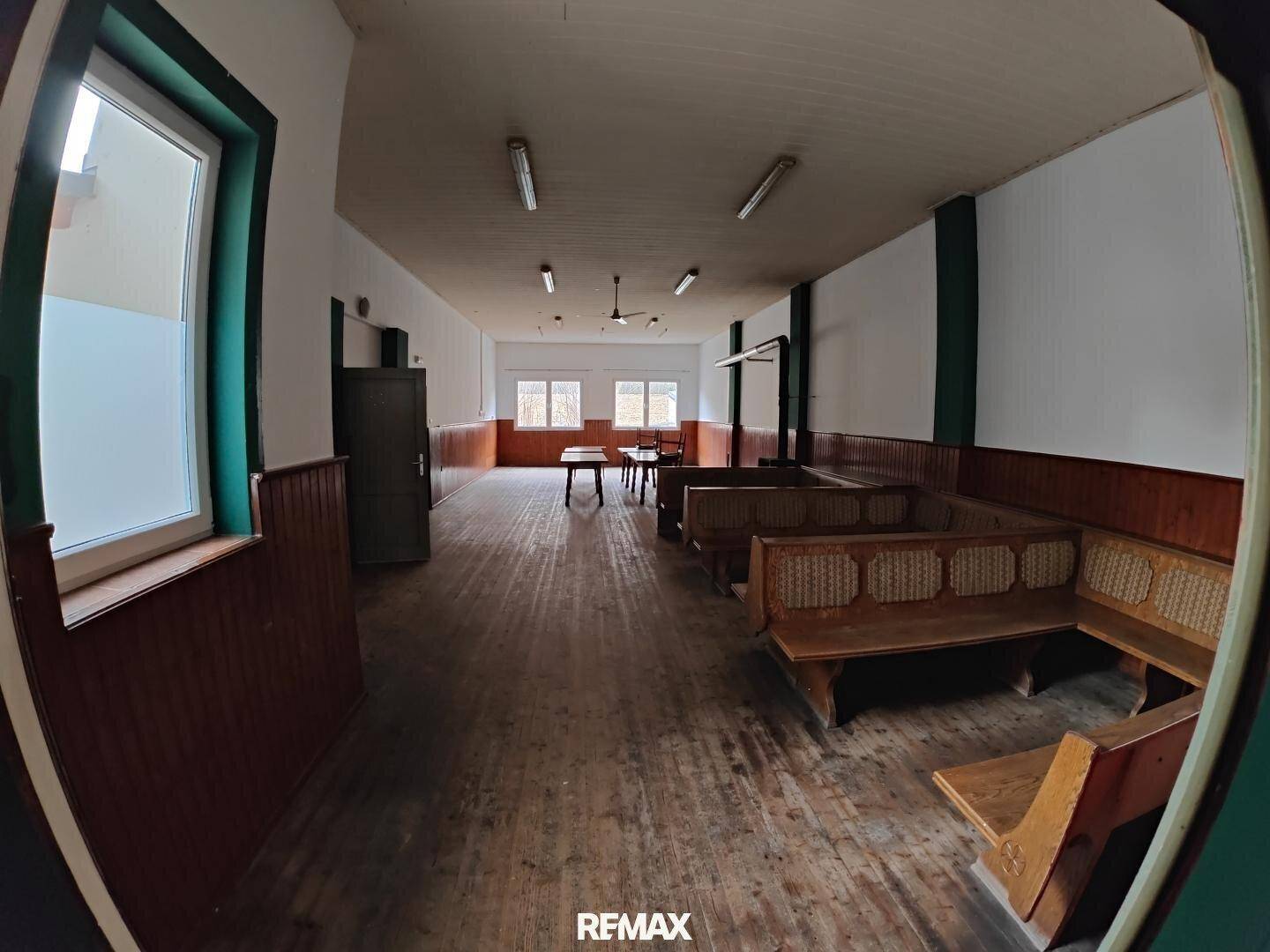 Großer Saal mit Holzbänken entlang der Wände und mehreren Tischen, ideal für Veranstaltungen.