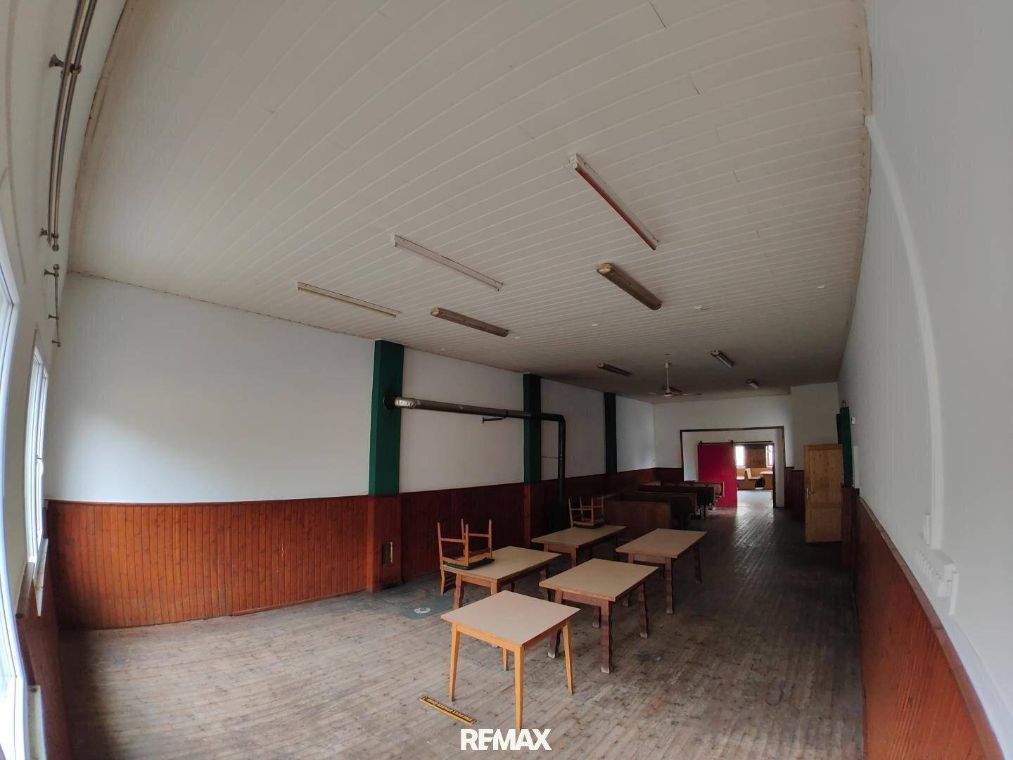 Geräumiger Saal mit Holztäfelung, mehreren Tischen und Stühlen, bereit für Gäste.