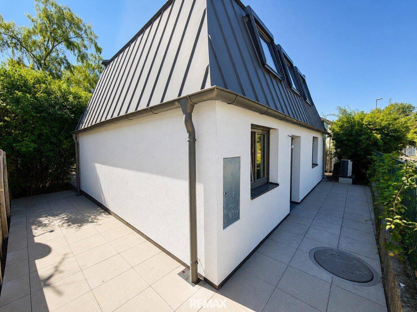 Seitliche Ansicht des Hauses mit einer gepflasterten Terrasse und moderner Fassadengestaltung.