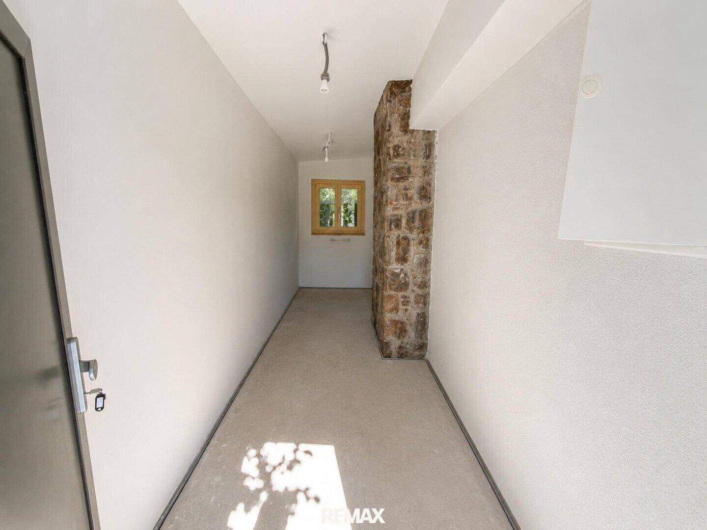 Langer, heller Flur mit einem Fenster und einer unverputzten Steinwand als Akzent.