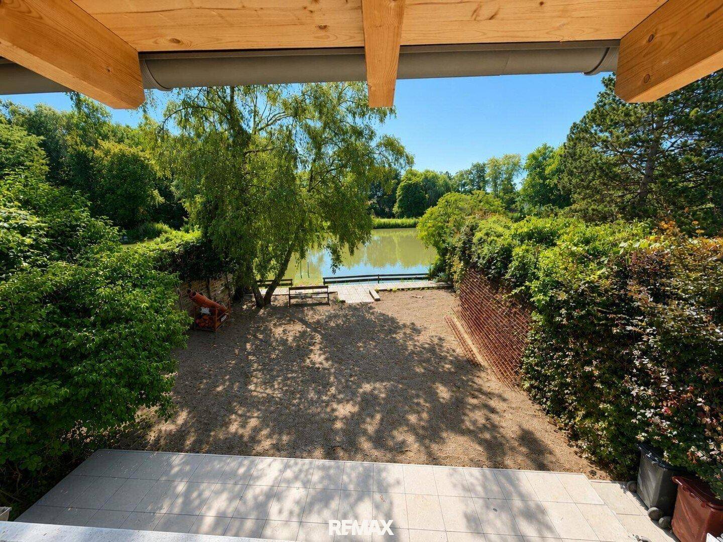 Panoramablick von oben auf den Gartenbereich und den angrenzenden See mit üppiger Vegetation.
