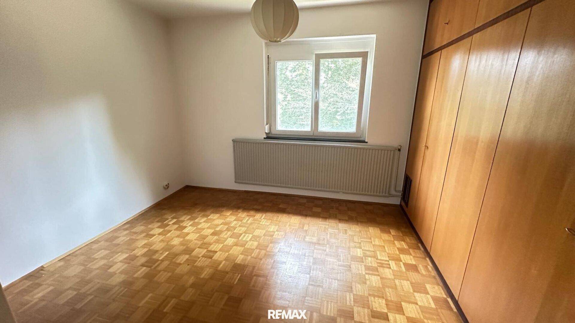 Schlafzimmer mit Parkettboden, eingebautem Holzschrank und einem Fenster für natürliches Licht.