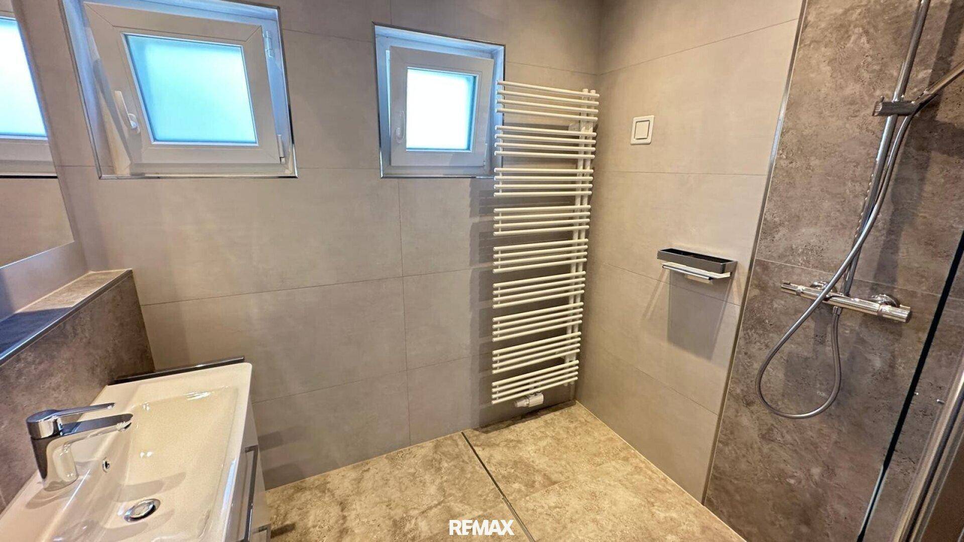 Modernes Badezimmer mit grauen Fliesen, ebenerdiger Dusche, Einzelwaschbecken und Handtuchheizkörper.