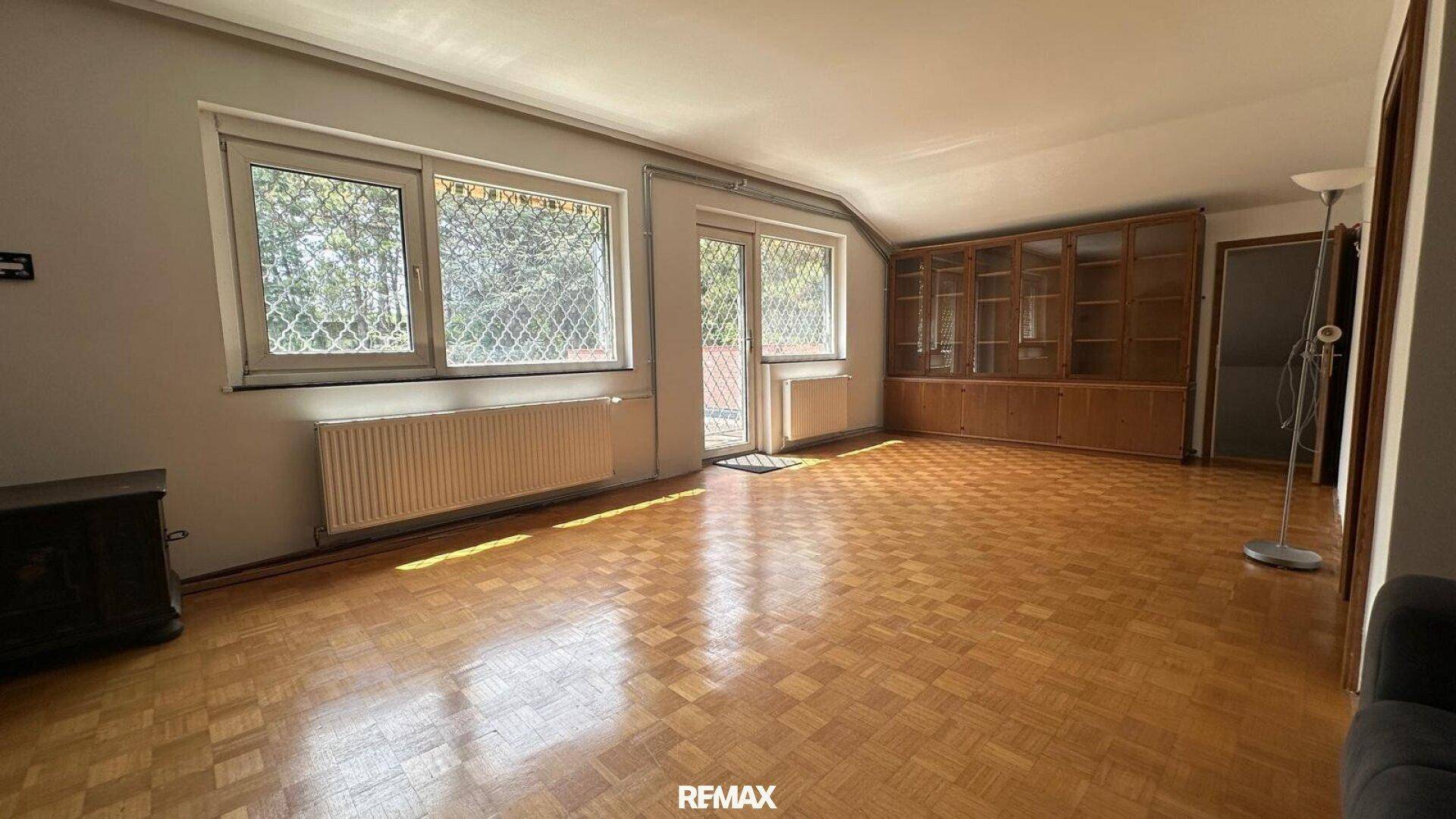 Geräumiges Wohnzimmer mit Parkettboden, großem Holzschrank und Zugang zu einem französischen Balkon.