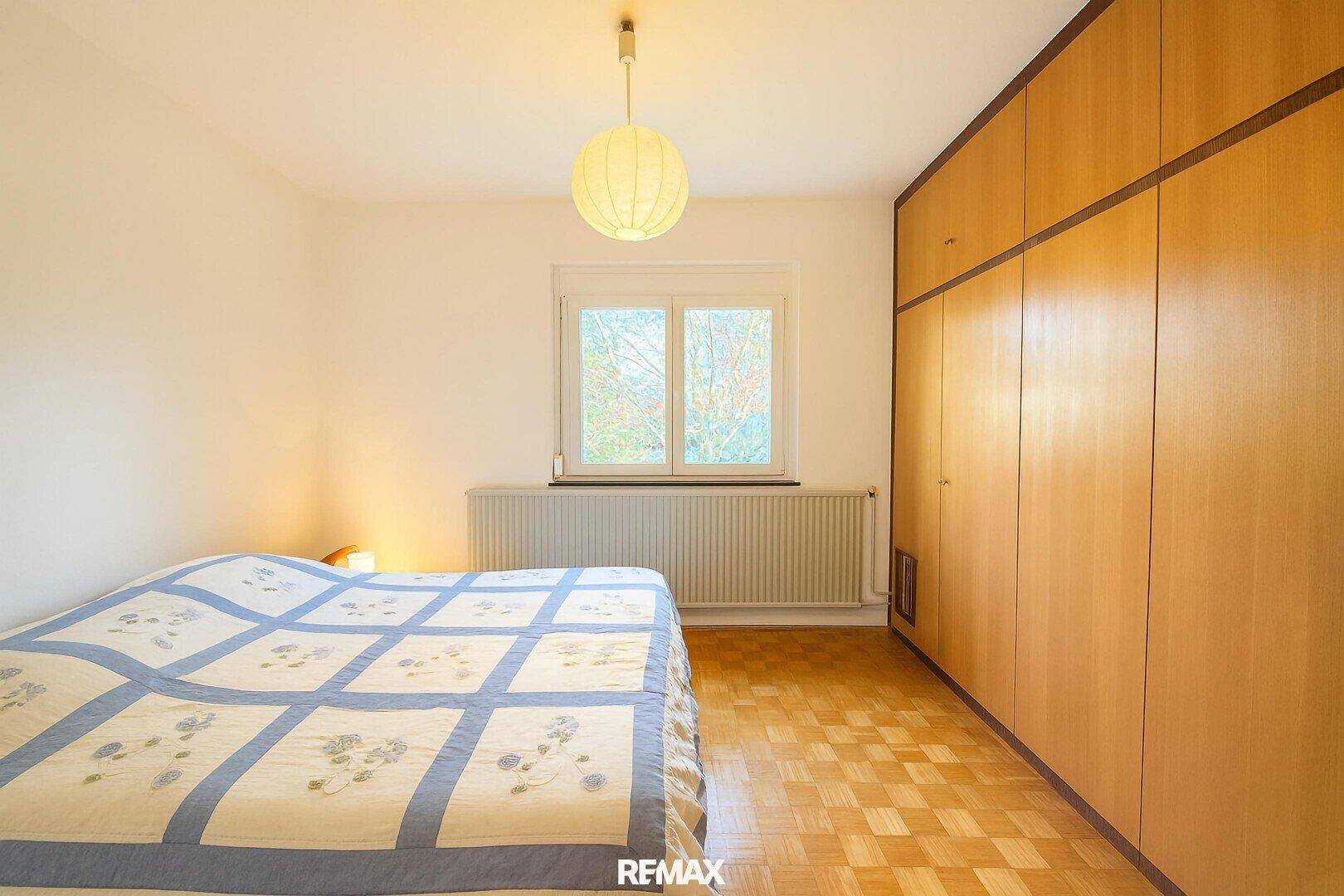 Schlafzimmer mit Parkettboden, einem Bett und einem großen, eingebauten Holzschrank.