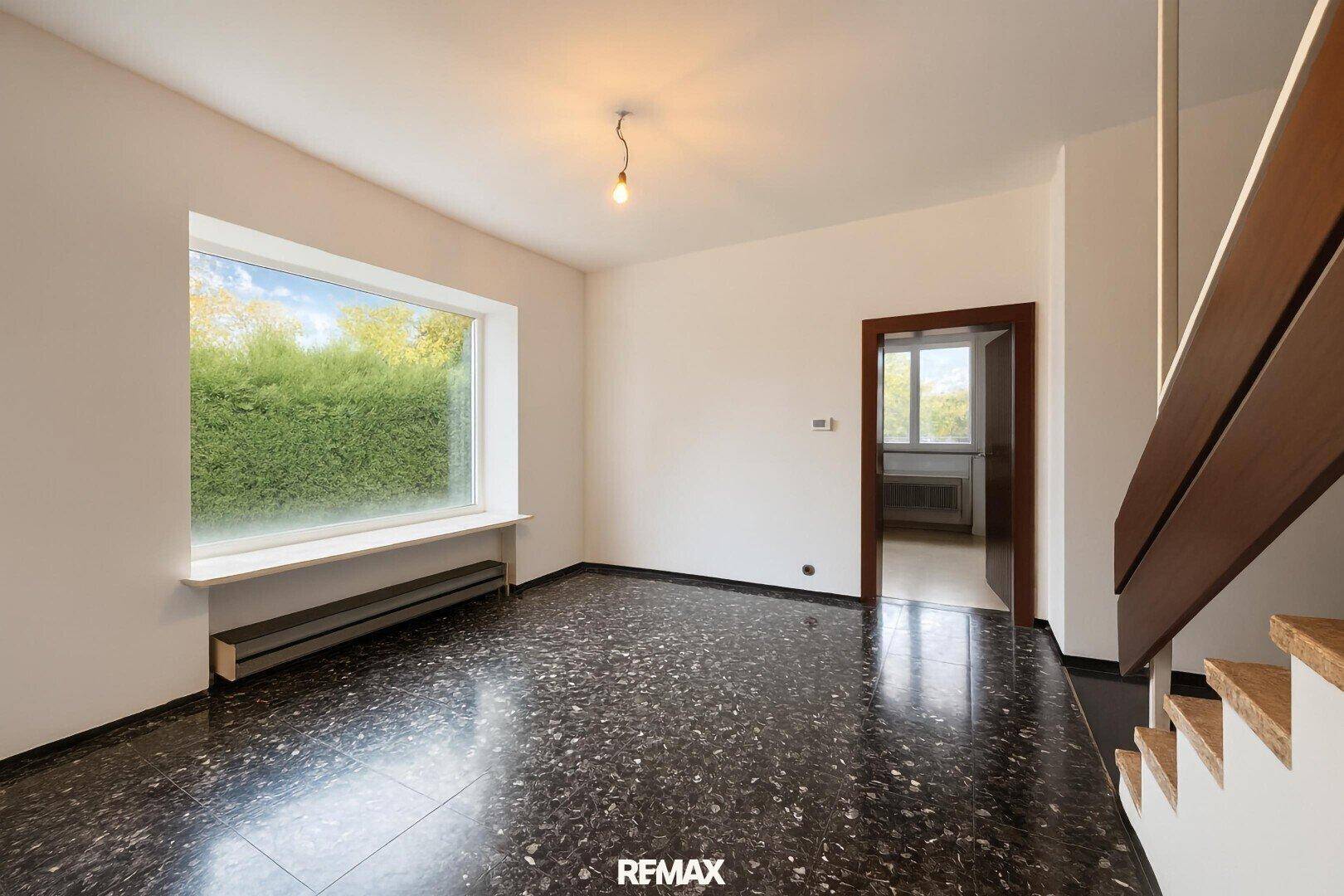 Heller Flur mit gemustertem Fliesenboden, großem Fenster und einer Holztreppe.