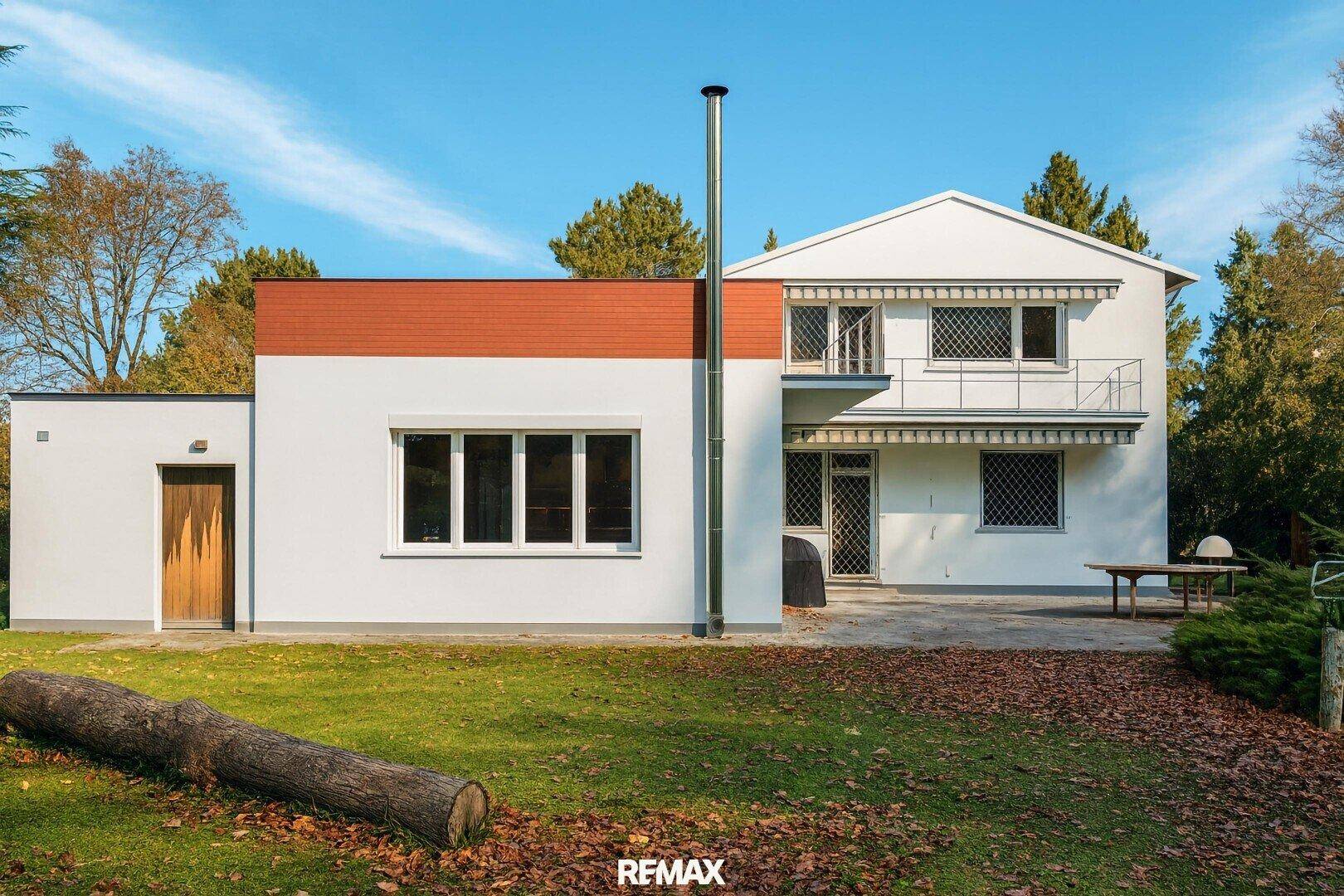 Rückseite des Hauses mit Garten, Rasenfläche und einem Balkon im Obergeschoss.