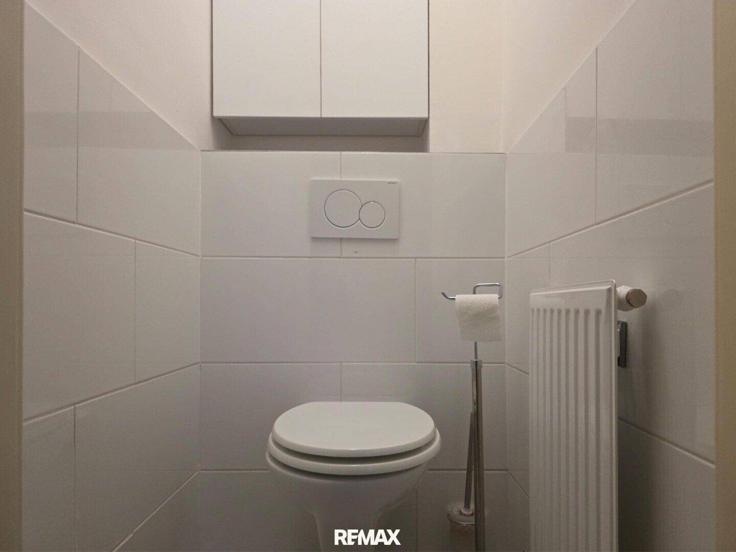 Separates WC mit wandhängender Toilette und weißen Fliesen für eine saubere Optik.