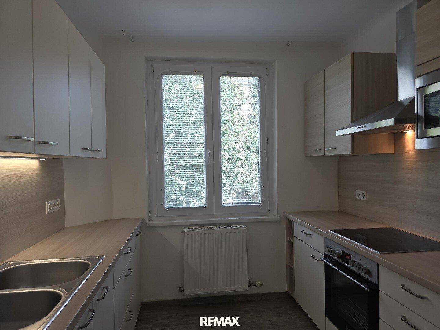 Funktionale Küche mit hellen Schränken, Holzoptik-Arbeitsplatten und Fenster zum grünen Außenbereich.