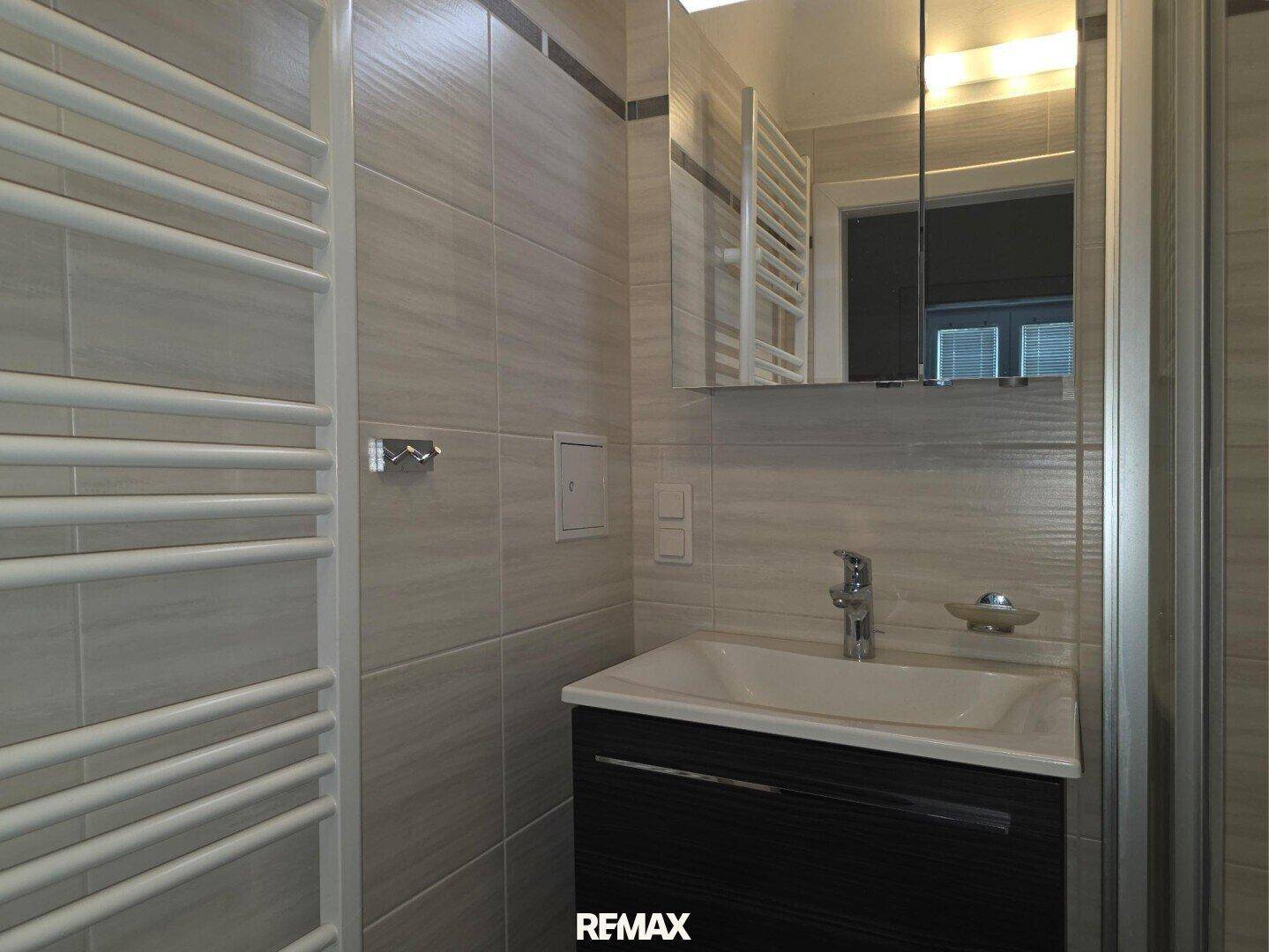 Badezimmer mit Waschbecken, Spiegelschrank und beheiztem Handtuchhalter an der gefliesten Wand.