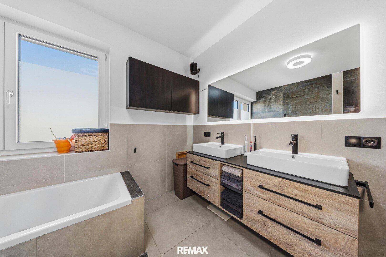 Modernes Badezimmer mit Doppelwaschbecken, großem Spiegel und Fenster.