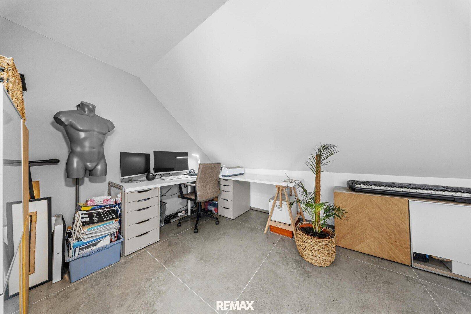 Helles Dachzimmer mit schräger Decke, eingerichtet als Arbeitsbereich mit Schreibtisch und Computern.