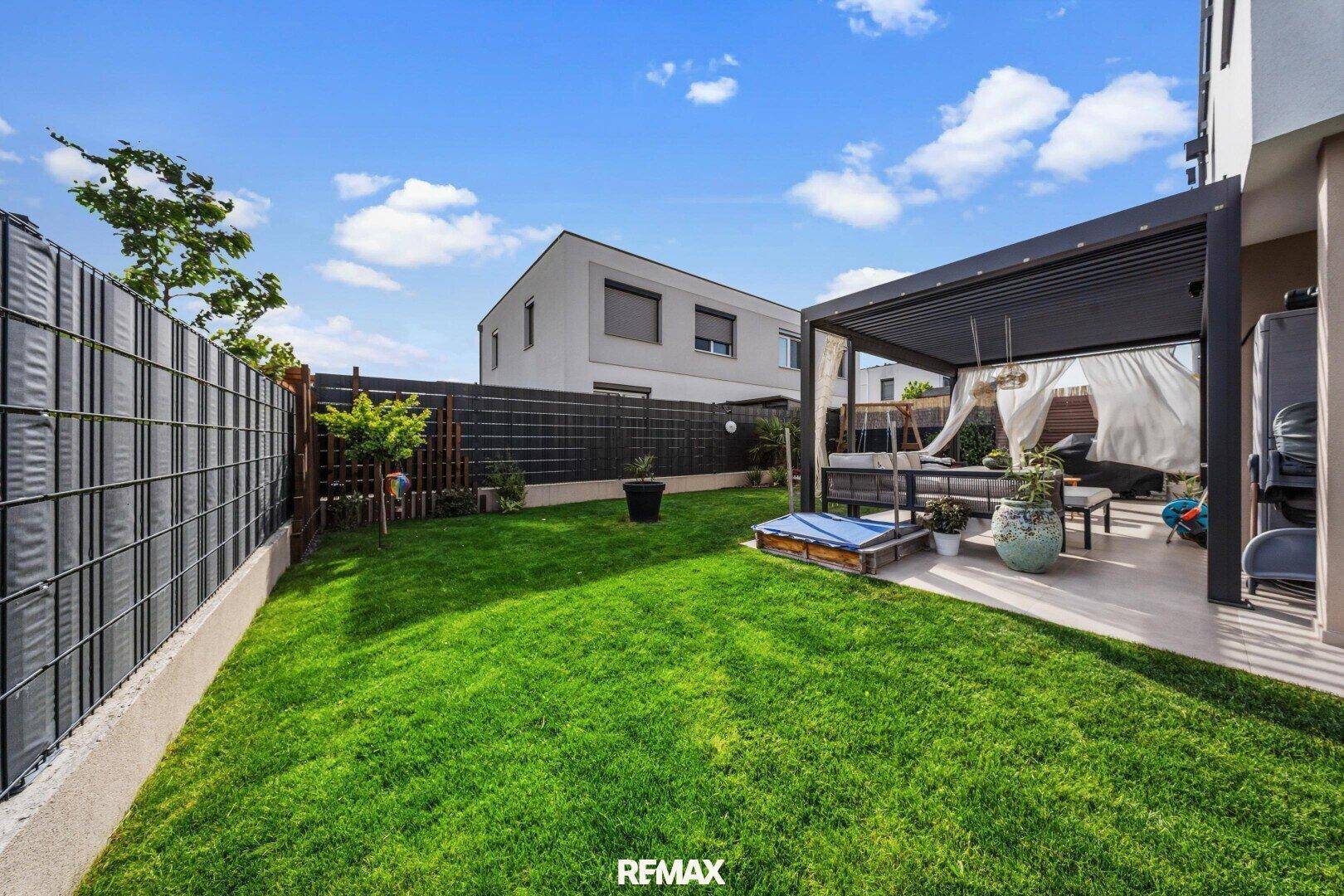 Grüner Garten mit Rasenfläche, Schaukel und einer überdachten Terrasse im Hintergrund.