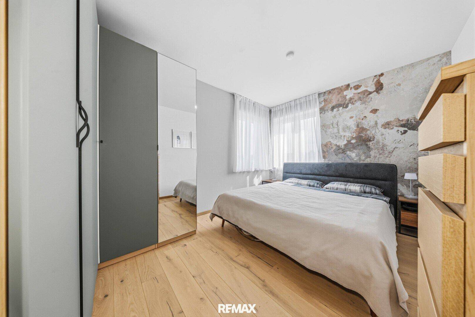 Helles Schlafzimmer mit Holzboden, großem Bett und modernem Kleiderschrank mit Spiegeltür.