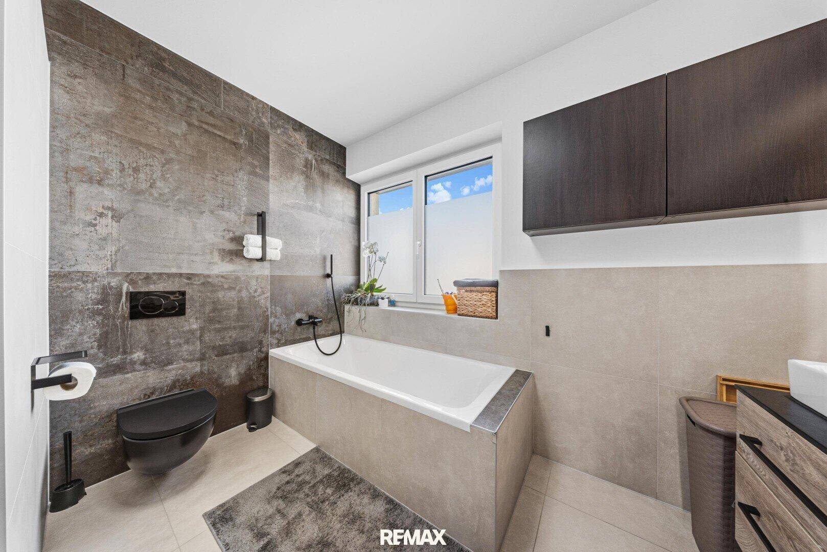 Modernes Badezimmer mit Badewanne, Wand-WC und großformatigen Fliesen.
