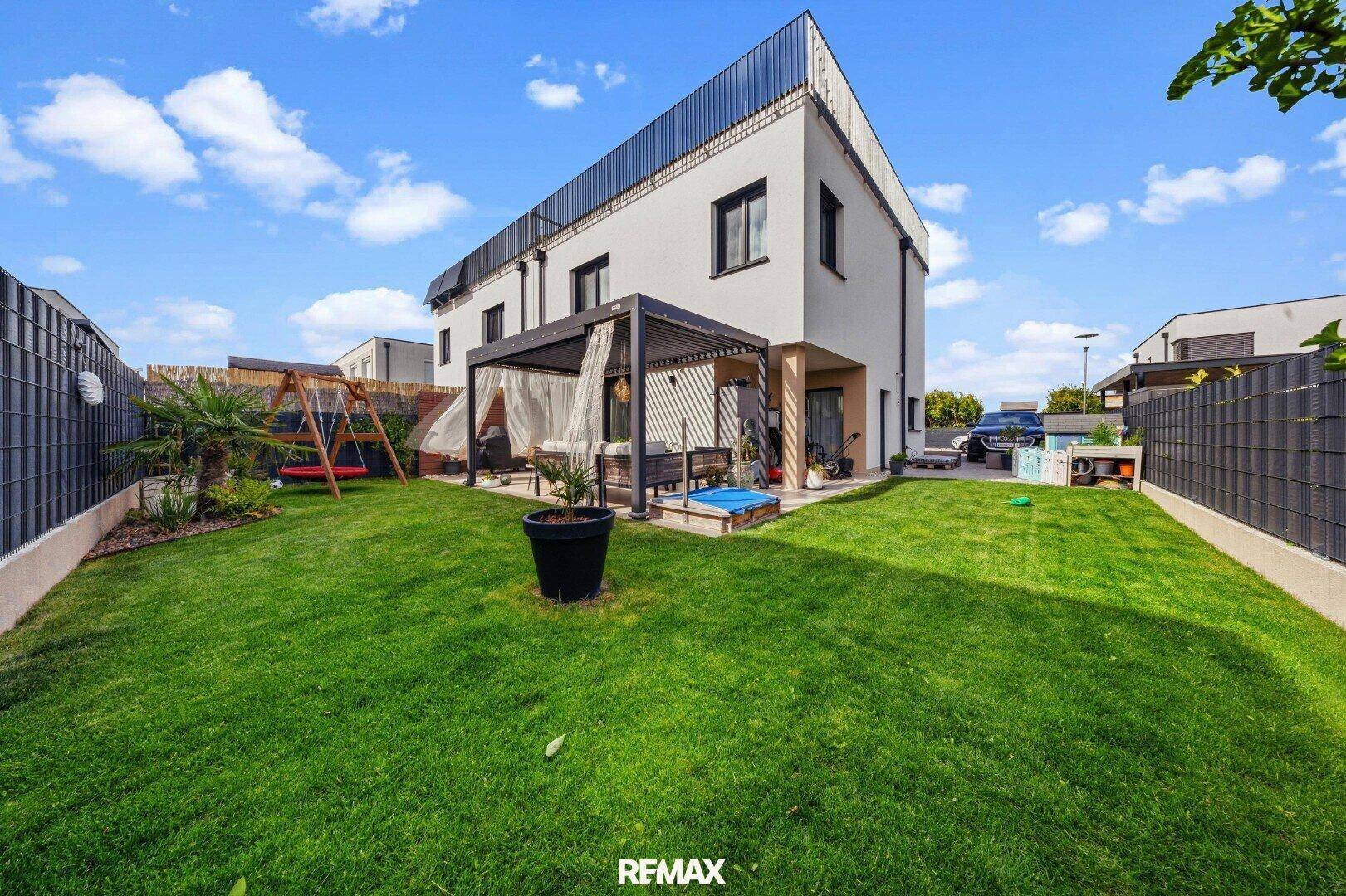 Gepflegter Gartenbereich mit Rasenfläche, Schaukel und moderner Hausfassade im Hintergrund.