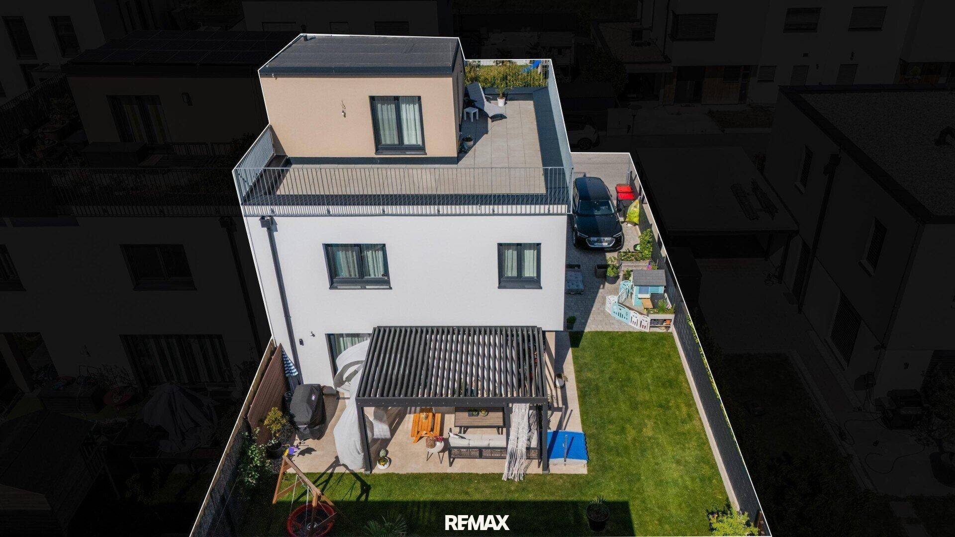 Moderne Wohnimmobilie aus der Vogelperspektive mit Garten, überdachter Terrasse und Dachterrasse.