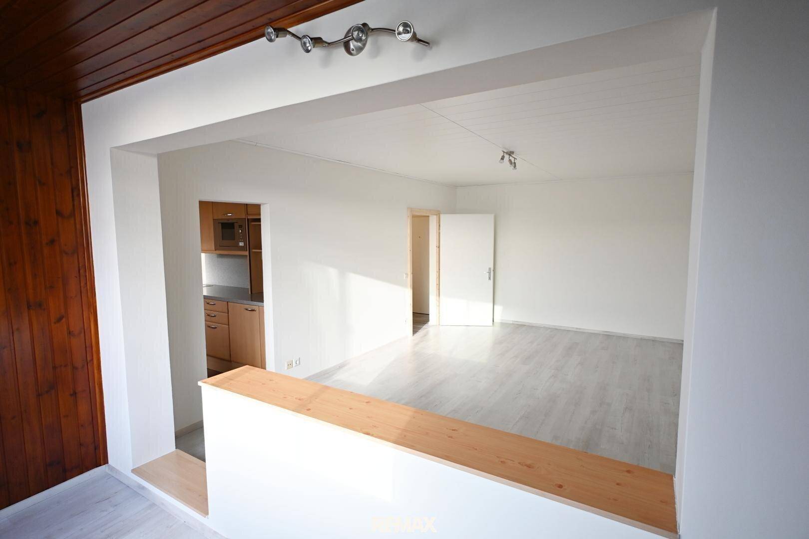 Blick in einen hellen Wohnbereich mit Laminatboden und Holzakzenten an Decke und Wand.