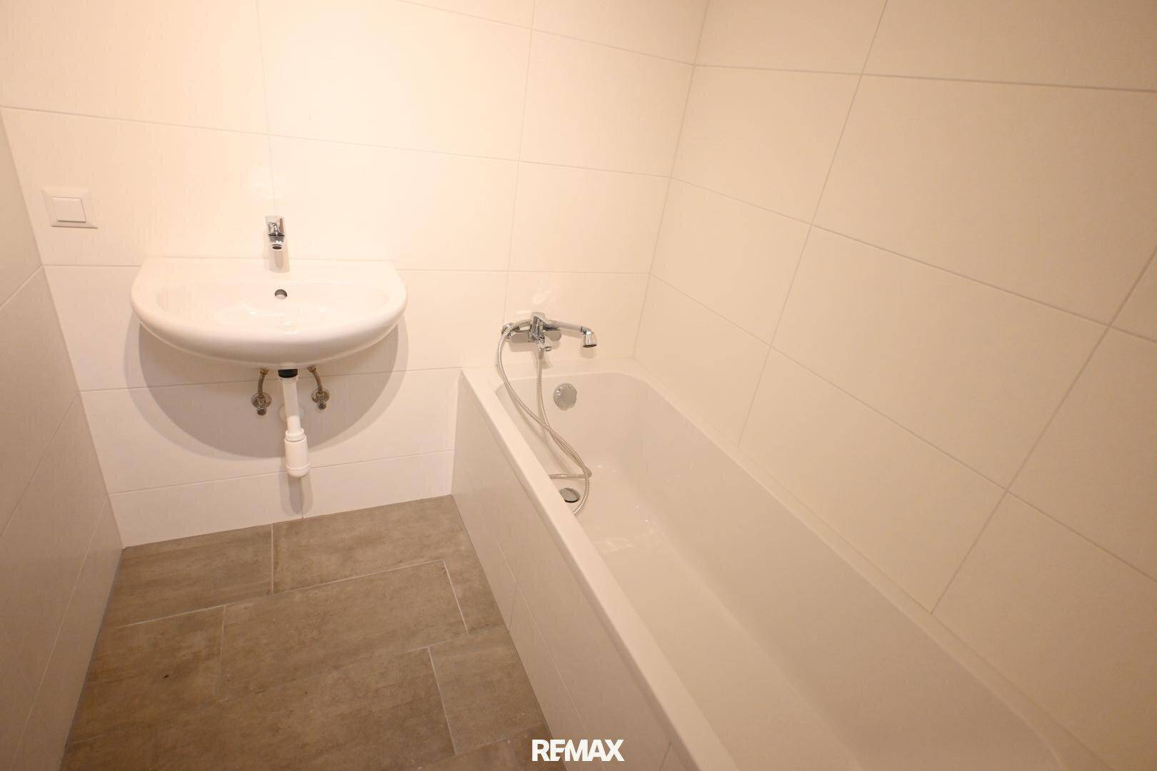 Modernes Badezimmer mit weißen Wandfliesen, grauen Bodenfliesen, Waschbecken und Badewanne.
