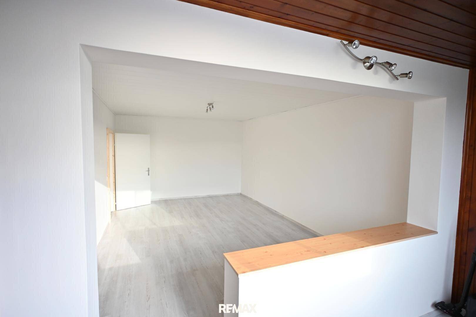 Offener Wohnbereich mit hellem Laminatboden und Holzelementen, der viel Tageslicht erhält.