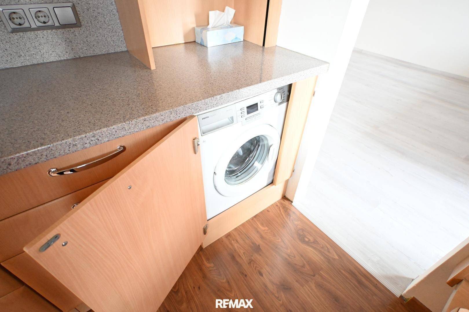 Integrierte Waschmaschine unter der Küchenarbeitsplatte in einer funktionalen Holzküche.