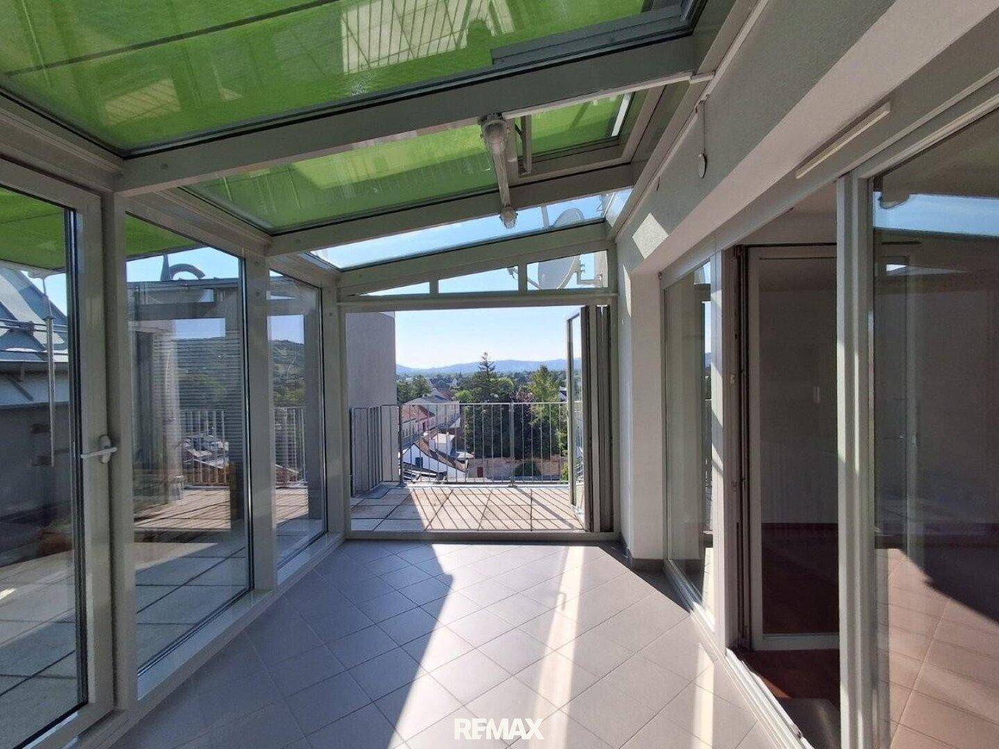 Heller Wintergarten mit Glasdach und Zugang zu einer Terrasse mit Weitblick über die Umgebung.
