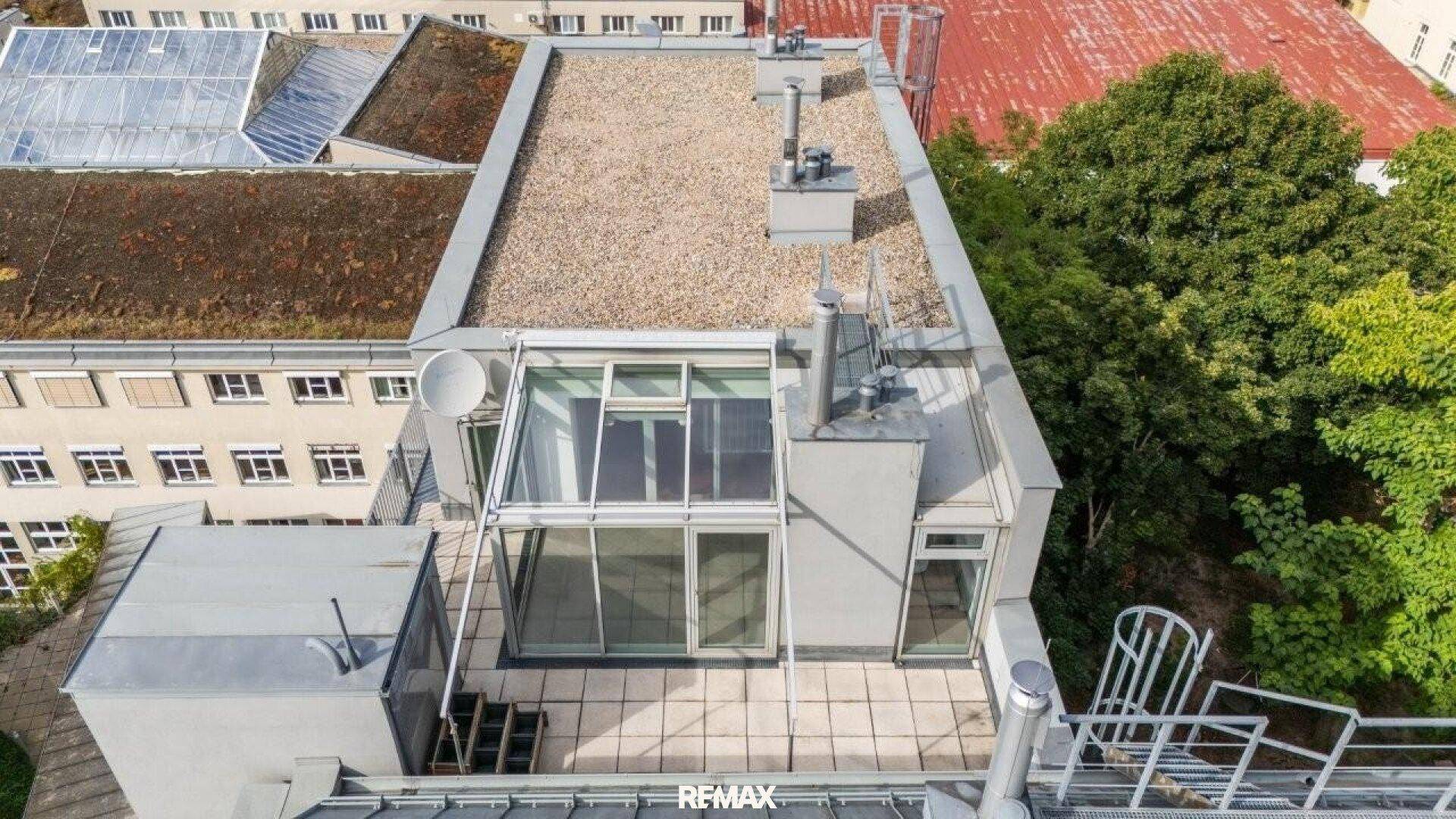 Geräumige Dachterrasse mit Glasüberdachung und Blick auf die umliegenden Gebäude.