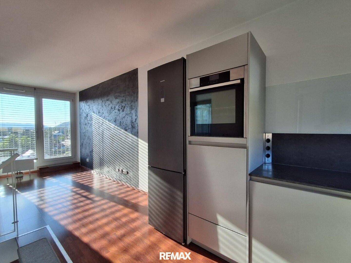 Moderne Küche mit integriertem Kühlschrank und Backofen, offen zum Wohnbereich.