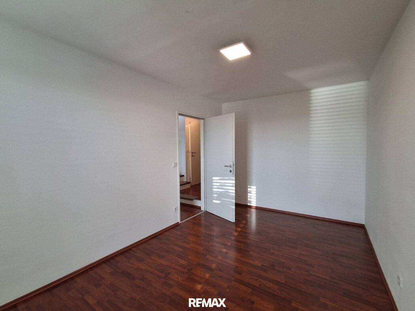 Leeres Schlafzimmer mit dunklem Laminatboden und weiß gestrichenen Wänden, bereit zur Einrichtung.