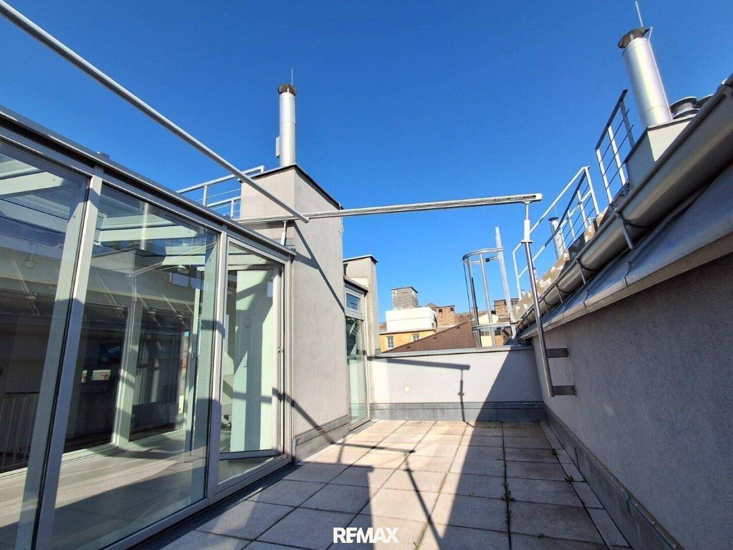 Geräumige Dachterrasse mit Fliesenboden und Geländer, angrenzend an einen Wintergarten.