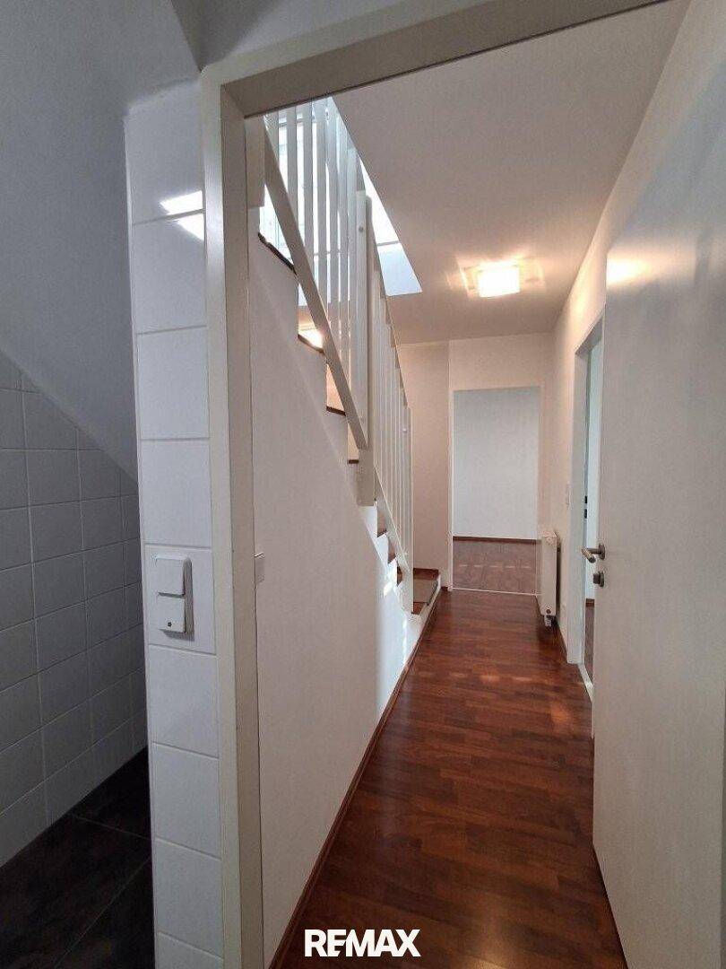 Heller Flur mit dunklem Laminatboden und einer Treppe, die in die obere Etage führt.