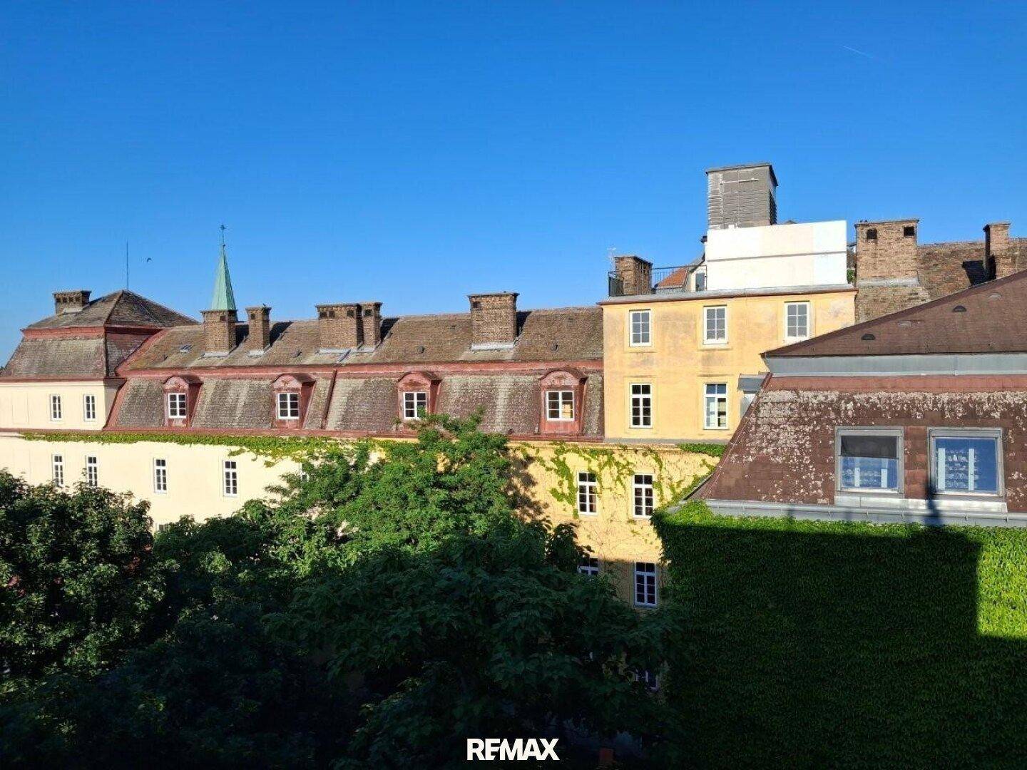 Historische Gebäude mit grünen Bäumen und einem klaren blauen Himmel im Hintergrund.