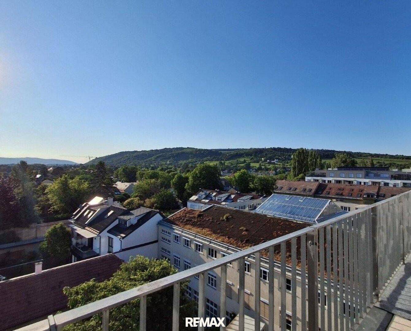 Panoramablick über grüne Hügel, Weinberge und die Dächer der umliegenden Häuser bei Sonnenschein.