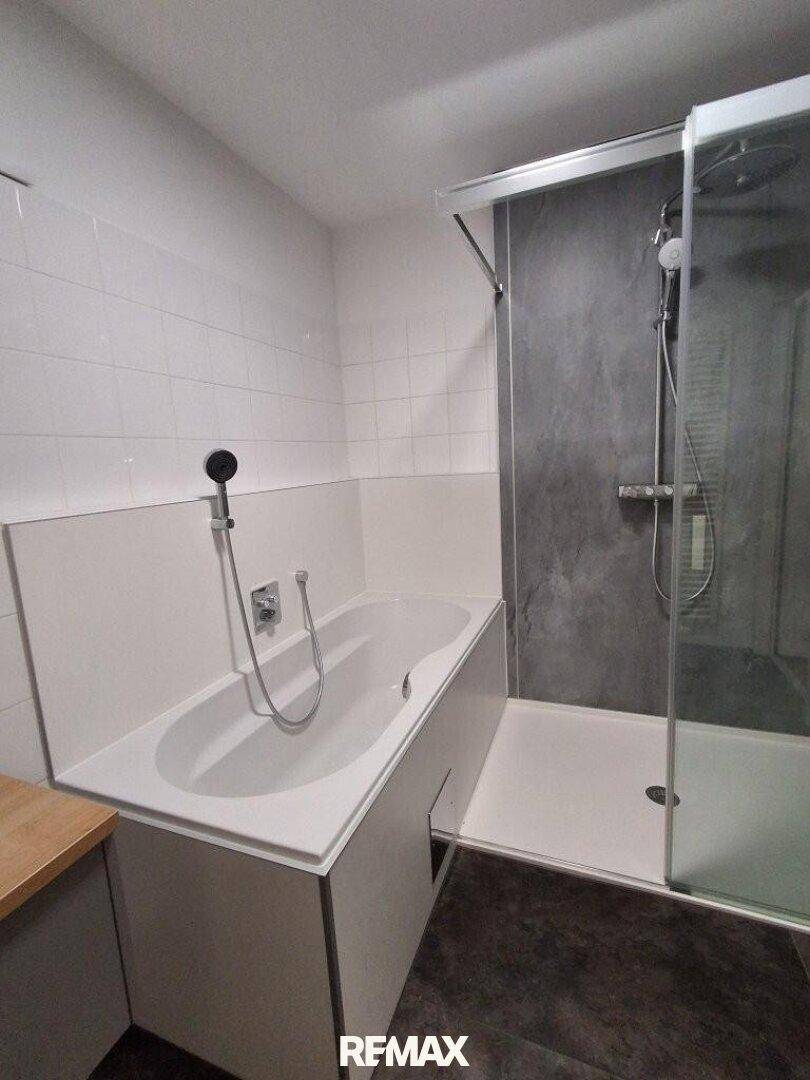 Badezimmer mit Badewanne und moderner begehbarer Dusche, ausgestattet mit weißen und grauen Fliesen.