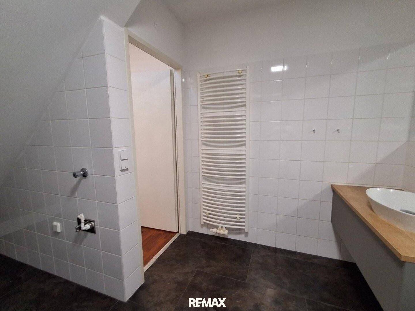 Modernes Badezimmer mit weißen Fliesen, Holzwaschtisch und beheiztem Handtuchhalter.