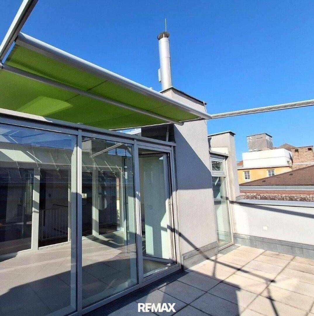 Dachterrasse mit angrenzendem Wintergarten und Blick auf die umliegenden Gebäude.