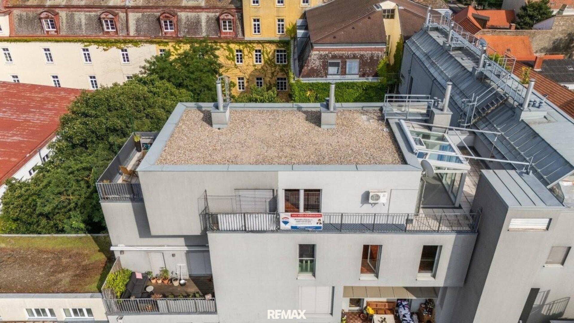 Luftaufnahme eines modernen Gebäudes mit Flachdach und Terrassen in städtischer Umgebung.