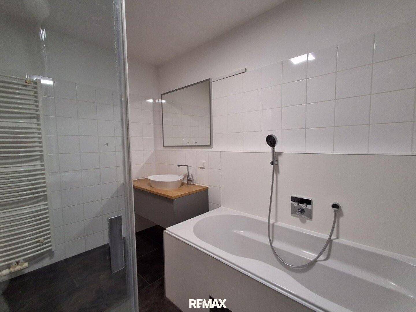 Modernes Badezimmer mit Badewanne, Duschbereich, Einzelwaschbecken und beheiztem Handtuchhalter.