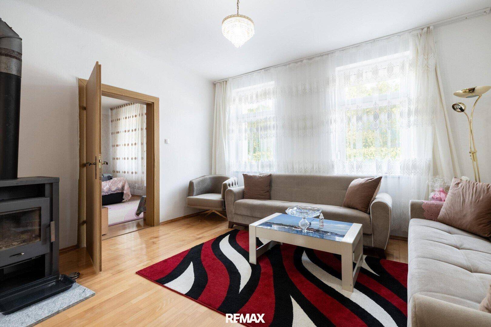 Gemütliches Wohnzimmer mit Holzofen, Parkettboden und hellem Tageslicht durch große Fenster.