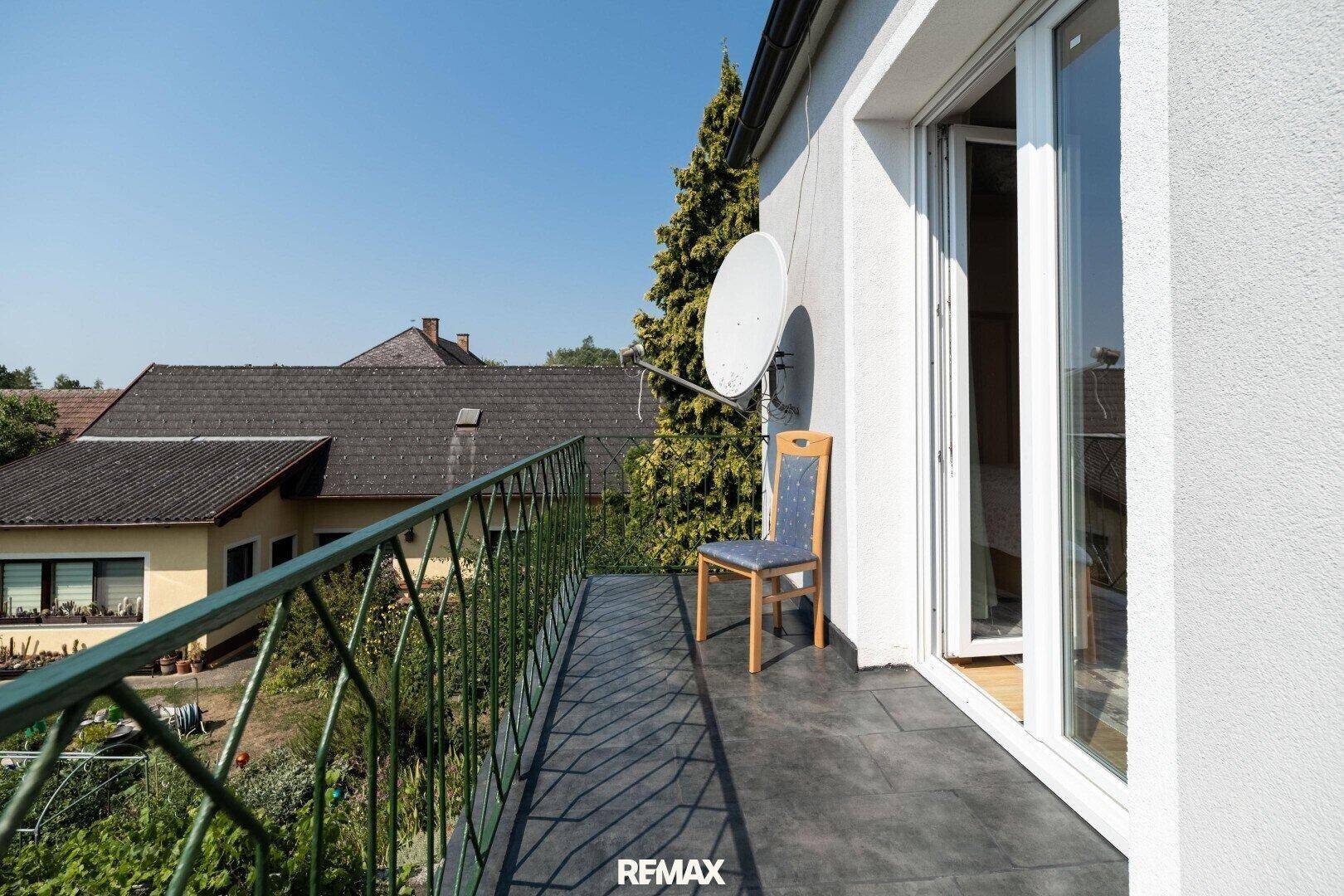 Schmaler Balkon mit Metallgeländer, einer Sitzgelegenheit und Satellitenschüssel.