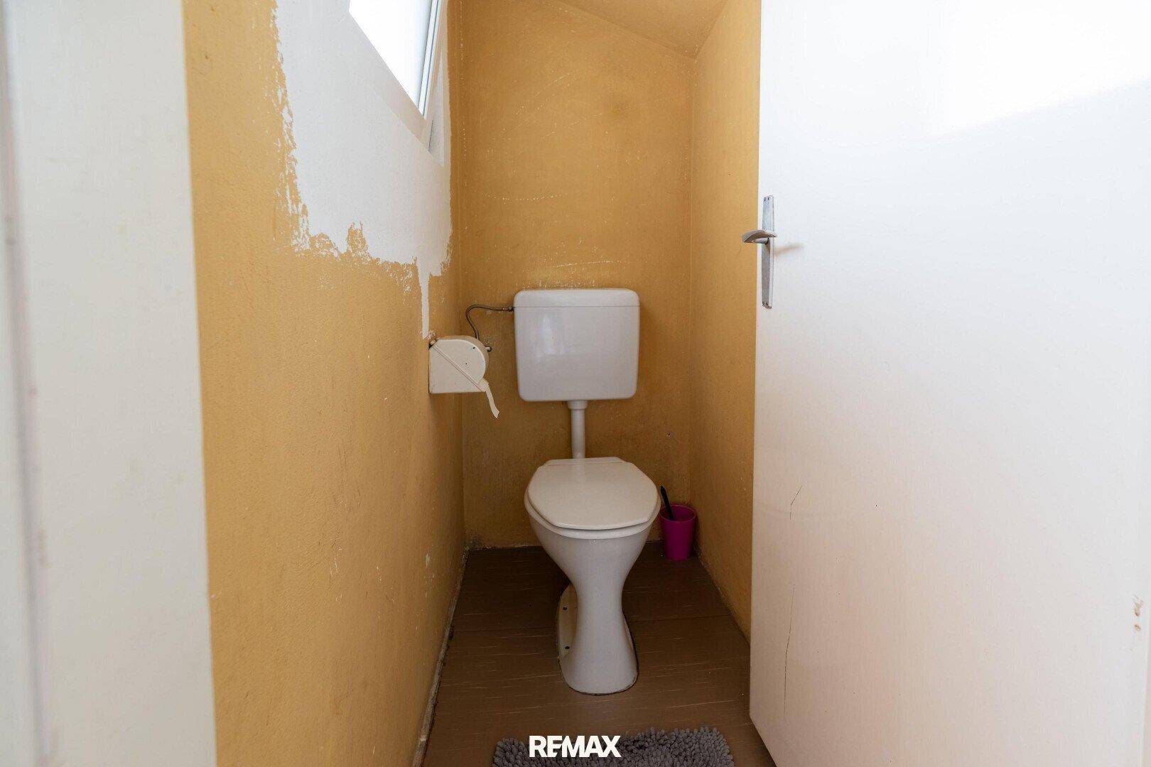 Separate Toilette mit WC und kleinem Fenster, Wände teilweise gelb gestrichen.