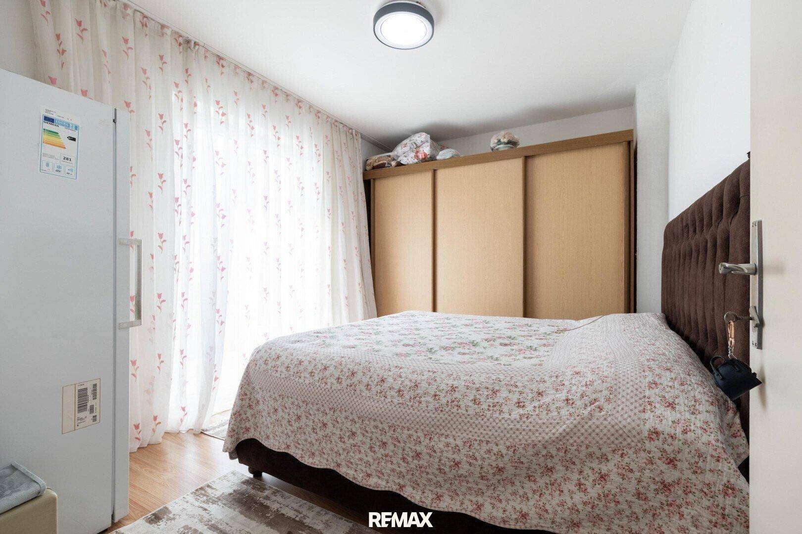 Schlafzimmer mit Doppelbett, Schiebetürenschrank und großem Fenster mit Vorhängen.