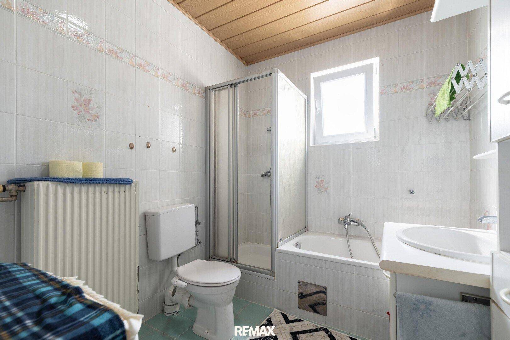 Badezimmer mit Badewanne, Duschkabine, WC und Fenster, gefliest in hellen Farben.